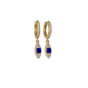 May include: A pair of gold-coloured hoop earrings, each adorned with small, clear crystals. Each earring features a teardrop-shaped pendant with a vibrant blue gemstone at its centre, encircled by smaller, clear crystals. The earrings are set against a white backdrop.