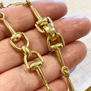 Pode incluir: Close-up de um colar de corrente dourada. A corrente apresenta uma s&eacute;rie de elos conectados com um design de freio de cavalo. Os elos s&atilde;o altamente polidos, refletindo a luz. O colar &eacute; provavelmente feito de metal.