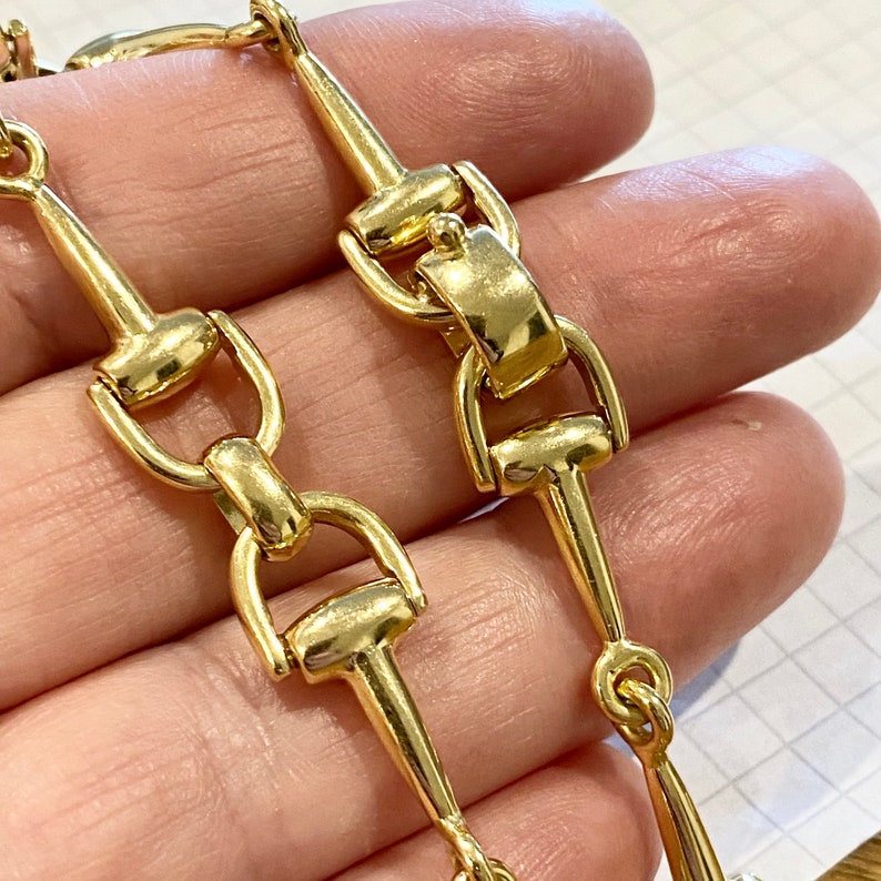 Pode incluir: Close-up de um colar de corrente dourada. A corrente apresenta uma s&eacute;rie de elos conectados com um design de freio de cavalo. Os elos s&atilde;o altamente polidos, refletindo a luz. O colar &eacute; provavelmente feito de metal.