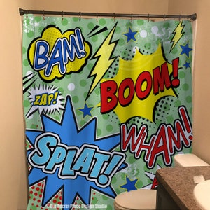 May include: A green shower curtain with a comic book theme. The shower curtain features colorful speech bubbles with the words "BAM!", "ZAP!", "BOOM!", "SPLAT!" and "WHAM!" in a retro style.
