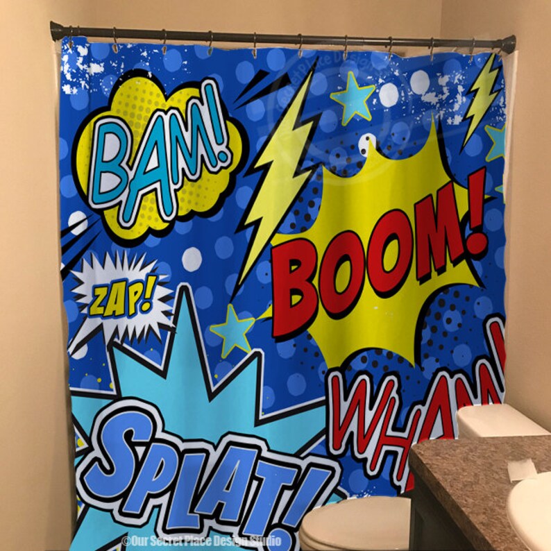 May include: A blue shower curtain with a comic book theme. The curtain features colorful speech bubbles with the words "BAM!", "ZAP!", "BOOM!" and "SPLAT!" in a bold, graphic font. The background is a blue and white polka dot pattern with yellow lightning bolts and stars.