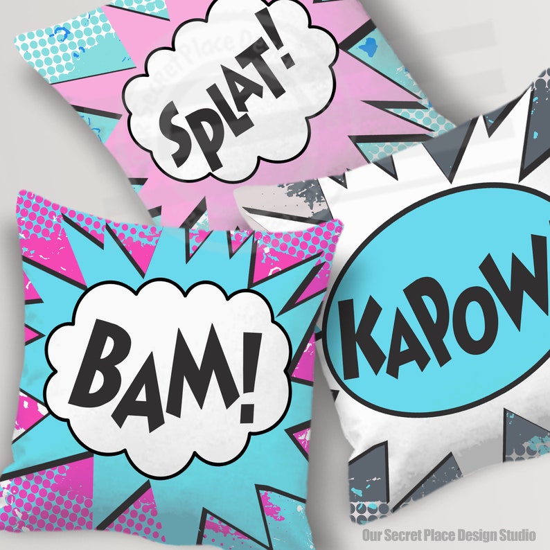 May include: Three decorative throw pillows with a comic book theme. The pillows are white with blue and pink accents. The pillows feature the words "BAM!" "KAPOW!" and "SPLAT!" in black text.