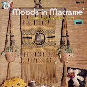 May include: A book cover with the title "Moods in Macrame' with Polypropylene Cord." The cover features a macrame wall hanging with a bell in the center, two macrame plant hangers, a macrame footstool, and a macrame table. The background is a woven brown material.