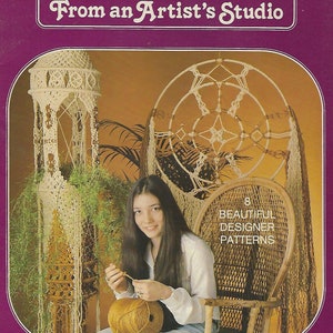 May include: A book cover with the title "Macrame From an Artist's Studio" in a purple and gold colour scheme. The cover features a woman sitting in a wicker chair, working on a macrame project. The book cover also features two macrame projects, a hanging plant holder and a dream catcher.
