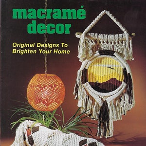 以下が含まれることがあります： 緑色の文字で「macramé decor」というタイトルが書かれた本の表紙。表紙には、夕焼けのシーンが描かれた壁掛けの装飾、吊り下げ式のランプシェード、長い枕など、マクラメのプロジェクトが3つ紹介されています。タイトルの下には「Original Designs To Brighten Your Home」というテキストが書かれています。