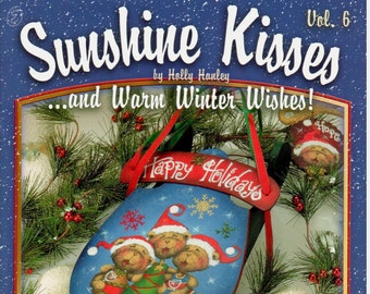 May include: A book cover with a blue background and a title that reads "Sunshine Kisses...and Warm Winter Wishes!"  The cover features a painted image of three bears on a sledge with a sign that reads "Happy Holidays".  The book is volume 6.