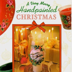 May include: A book titled "A Very Merry Handpainted Christmas" by Carol Mays. The cover features a hand-painted candle holder with a winter scene, surrounded by candles and other festive decorations.