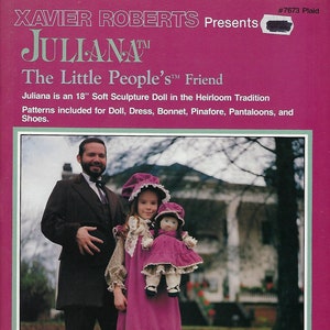 Könnte beinhalten: Eine rosa und weiße Puppe mit einem rosa Kleid und einer weißen Haube. Die Puppe hält eine kleinere Puppe mit einem rosa Kleid und einer weißen Haube. Die Puppen stehen vor einem Mann in einem dunklen Anzug. Das Bild enthält den Text "JULLANA™ The Little People's™ Friend".