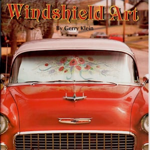 Op de afbeelding: Een rode vintage auto met een op maat geschilderde windschermzonnescherm met een bloemenmotief. De auto heeft een chromen bumper en een kentekenplaat met de tekst "I PAINT" met de staat Missouri. De titel van het boek is "Windshield Art" door Gerry Klein.