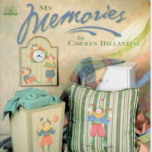 Peut inclure: Un livre intitulé "My Memories" de Carolyn Ballantine, illustrant des clowns jonglant avec des balles et une horloge avec un visage de clown. La couverture du livre est décorée d'un coussin rayé vert et blanc, d'une serviette verte et d'une boîte blanche.