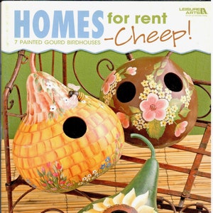 May include: Seven painted gourd birdhouses, each with a unique design. The birdhouses are displayed on a wooden rack with a brown background. The text "Homes for rent -Cheep!" is printed on the front of the book.  7 Painted Gourd Birdhouses.