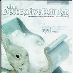 Puede incluir: Un trineo de madera pintado de azul y blanco con un conejo blanco en su interior. El trineo está decorado con pintura dorada y tiene un fondo blanco. El texto "Arctic Legend" está escrito en letras negras en el trineo. El texto "Paint a Peggy Harris Snow Bunny on an Heirloom Sleigh Page 90" está escrito en letras negras en el lado derecho de la imagen.