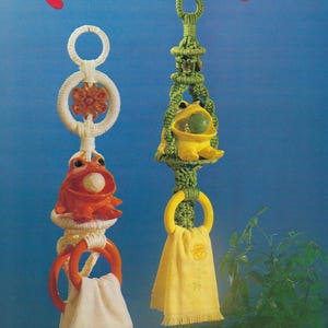 May include: Macramé Festival image featuring two handmade towel holders. One is orange with a white towel, the other is green with a yellow towel. The text "Macramé Festival" is in red script at the top.
