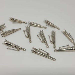 May include: A group of 12 silver-toned metal cone-shaped brooches with a pin closure. The brooches have a decorative design on the surface.