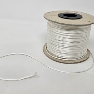 May include: A spool of white satin cord, with a length of cord extending from the spool.