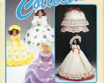 May include: A book cover featuring a collection of doll projects. The cover shows three dolls dressed in different styles, including a white dress with lace, a purple dress with lace, and a yellow dress with daisies. The book title is "Doll Collection" and the subtitle is "A Doll for Everyone! 13 Wonderful Doll Projects for You from Taurus".