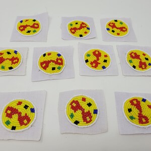 May include: Ten round, colorful beaded patches on white fabric squares. Each patch features a red, yellow, and blue design with a white background.