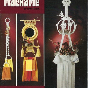 Könnte beinhalten: Ein Vintage-Buchcover für ein Makramee-Handwerksprojekt. Das Cover zeigt drei Makramee-Projekte: einen Hängekorb, einen Wandspiegel und einen Handtuchhalter. Der Buchtitel lautet "Makramee" von Lynn Paulin. Der Text "Einfach Elegant Praktisch" ist über dem Titel gedruckt. Das Buchcover ist rot mit einem weißen Rand.