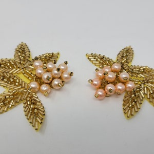 May include: Two gold leaf-shaped embellishments with pink pearl clusters. Each embellishment features a cluster of pink pearls in the center, surrounded by gold beads arranged in a leaf shape.