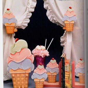 May include: Wooden ice cream cone decorations in various sizes, with pastel scoops and a cherry on top. The cones are brown, and the scoops are pink, blue, and green. The text "ICE CREAM DREAMS" is visible.