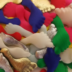 Puede incluir: Una colección de formas de pies de fieltro de colores en varios colores, incluyendo rojo, azul, verde, blanco, dorado y plateado. Las formas son todas aproximadamente del mismo tamaño y tienen una superficie ligeramente texturizada.