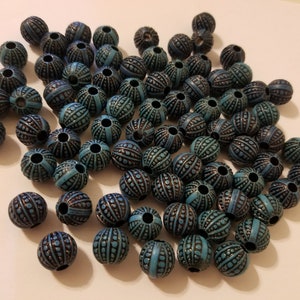 May include: A large pile of round, blue and black beads with a textured surface. The beads have a hole in the center for stringing.