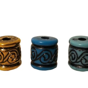 May include: Three barrel-shaped beads in gold, blue, and teal. Each bead features a dark, swirling pattern around the body. The beads have a hole through the center, suitable for stringing. These decorative beads are ideal for jewelry making.