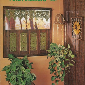 May include: A book titled "Macrame Ideas And Answers" with the subtitle "Book 1" on the cover. The cover features a macrame window valance, a macrame hanging plant holder, and a macrame wall hanging. The book is set against a wood-paneled wall.