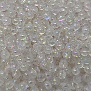 May include: A close-up of a pile of iridescent white glass beads. The beads are round and have a smooth, shiny finish.