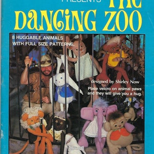 Könnte beinhalten: Ein blauer Buchumschlag mit dem Titel "The Dancing Zoo" von Xavier Roberts. Der Umschlag zeigt ein Foto eines Mannes in Safari-Kleidung mit acht Stofftieren in einem Käfig. Das Buch enthält Schnittmuster in Originalgröße zum Nähen der Stofftiere.