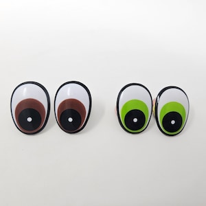 Könnte beinhalten: Zwei Paare von Glitz Augen, ein Paar mit braunen Iris und ein Paar mit grünen Iris. Die Augen sind weiß mit schwarzen Pupillen und aus Kunststoff.