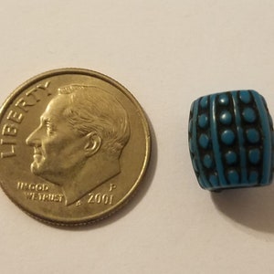 Puede incluir: Una cuenta de vidrio azul turquesa con un patr&oacute;n geom&eacute;trico en blanco y negro. La cuenta es aproximadamente del tama&ntilde;o de una moneda de diez c&eacute;ntimos.