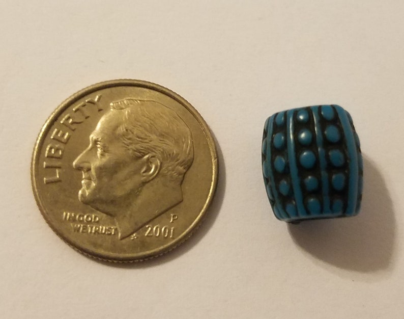 Puede incluir: Una cuenta de vidrio azul turquesa con un patr&oacute;n geom&eacute;trico en blanco y negro. La cuenta es aproximadamente del tama&ntilde;o de una moneda de diez c&eacute;ntimos.