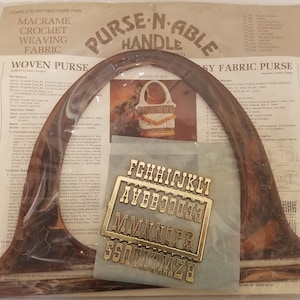 May include: A brown plastic purse handle with a marbled pattern. The handle is shaped like a half-circle and has a metal alphabet chart attached to it. The text on the chart reads "FGHHIJJKLT AYBBCCJDEE MMNNOPR SSOTTXXMZH".