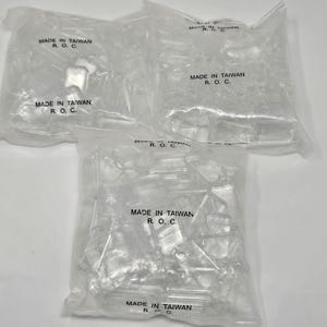 May include: Three clear plastic bags filled with small, transparent rectangular components. Each bag is sealed and features the black printed text MADE IN TAIWAN R. O. C. repeated on the surface. The contents appear to be uniform, rigid, and colorless plastic pieces.
