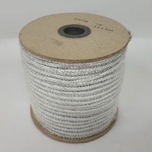 Könnte beinhalten: Eine Rolle silberfarbenes Metallic-Band. Das Band ist um einen Pappkern gewickelt. Auf der Rolle steht "144 YDS". Das Band eignet sich für Bastelarbeiten, Geschenkverpackungen oder dekorative Zwecke. Ungefähr 131 Meter.