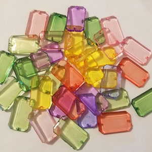 May include: A pile of colorful, translucent, rectangular-shaped plastic gems. The gems are in various shades of green, yellow, orange, pink, and purple.