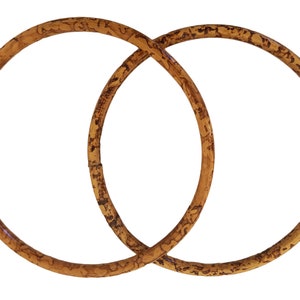 Könnte beinhalten: Zwei ineinander verschlungene braune Bambusringe. Die Ringe sind glatt und haben eine natürliche Holzmaserung.