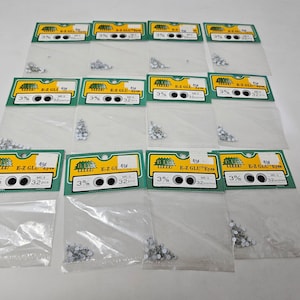 May include: Ten packages of small, white, self-adhesive plastic eyes. Each package contains 32 eyes and is labeled "E-Z GLU Eyes" with a green background and black text. The packages are arranged in three rows.