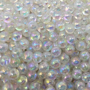 Può includere: Primo piano di perline di vetro bianche iridescenti. Le perline sono rotonde e hanno una finitura liscia e lucida.