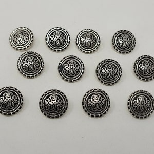 May include: Twelve silver-toned metal buttons with an intricate design. Each button is round and has a raised, detailed pattern.