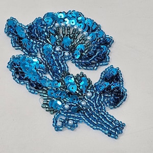 May include: A blue and white beaded flower applique. The flower is made of small, round beads and has a delicate, feminine look.
