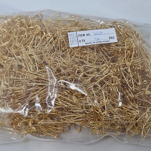 May include: A clear plastic bag filled with a large quantity of gold safety pins. The bag has a label that reads "ITEM NO. 3218 QTY 512 DOZ. MADE IN HONG KONG."