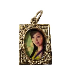 May include: A silver charm with a photo of a woman in an oval frame. The frame has a decorative design with floral accents.