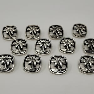 May include: Twelve silver-toned metal buttons with a palm tree design. Each button is square-shaped with rounded corners.