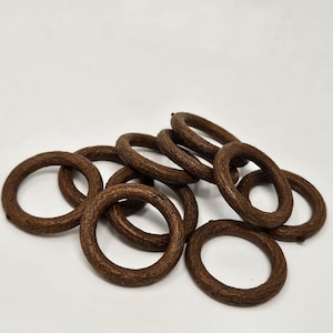 Puede incluir: Un montón de anillos de cortina de madera marrón. Los anillos están hechos de madera natural y tienen una superficie rugosa y texturizada.