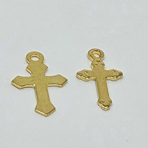 May include: Two gold-colored metal cross charms. The cross on the left has a simple design, while the cross on the right has a more ornate design with small details around the edges.