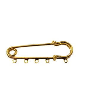 May include: Gold-toned safety pin with five jump rings attached to the bottom. The safety pin is open and ready to be used.
