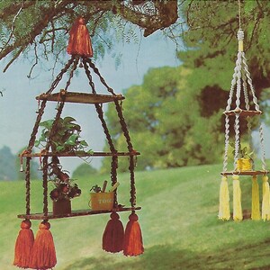 May include: Two macrame plant hangers with wooden shelves. The larger hanger has three shelves and is decorated with red tassels. The smaller hanger has two shelves and is decorated with yellow tassels.