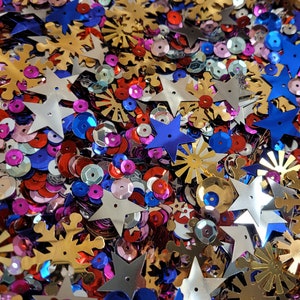 May include: A mix of colorful sequins in red, blue, silver, and gold. The sequins are shaped like stars, snowflakes, and circles.